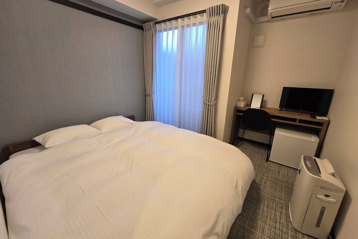A hotel room with a large bed, a desk with a computer, a TV, and an air conditioner.