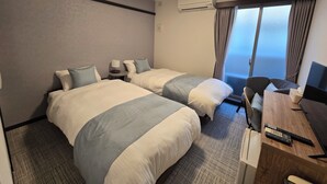 Une chambre d’hôtel avec deux lits, un bureau, une chaise, une lampe, un climatiseur et une fenêtre avec des rideaux.