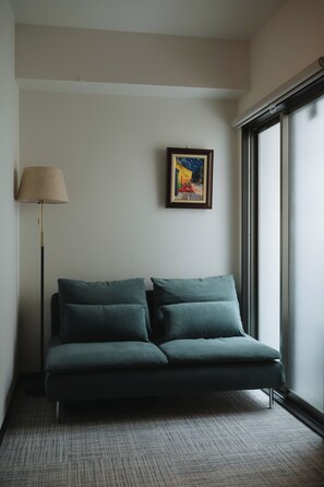 Ein modernes Zimmer mit einer Couch, einer Lampe, einem Gemälde und einem großen Fenster.