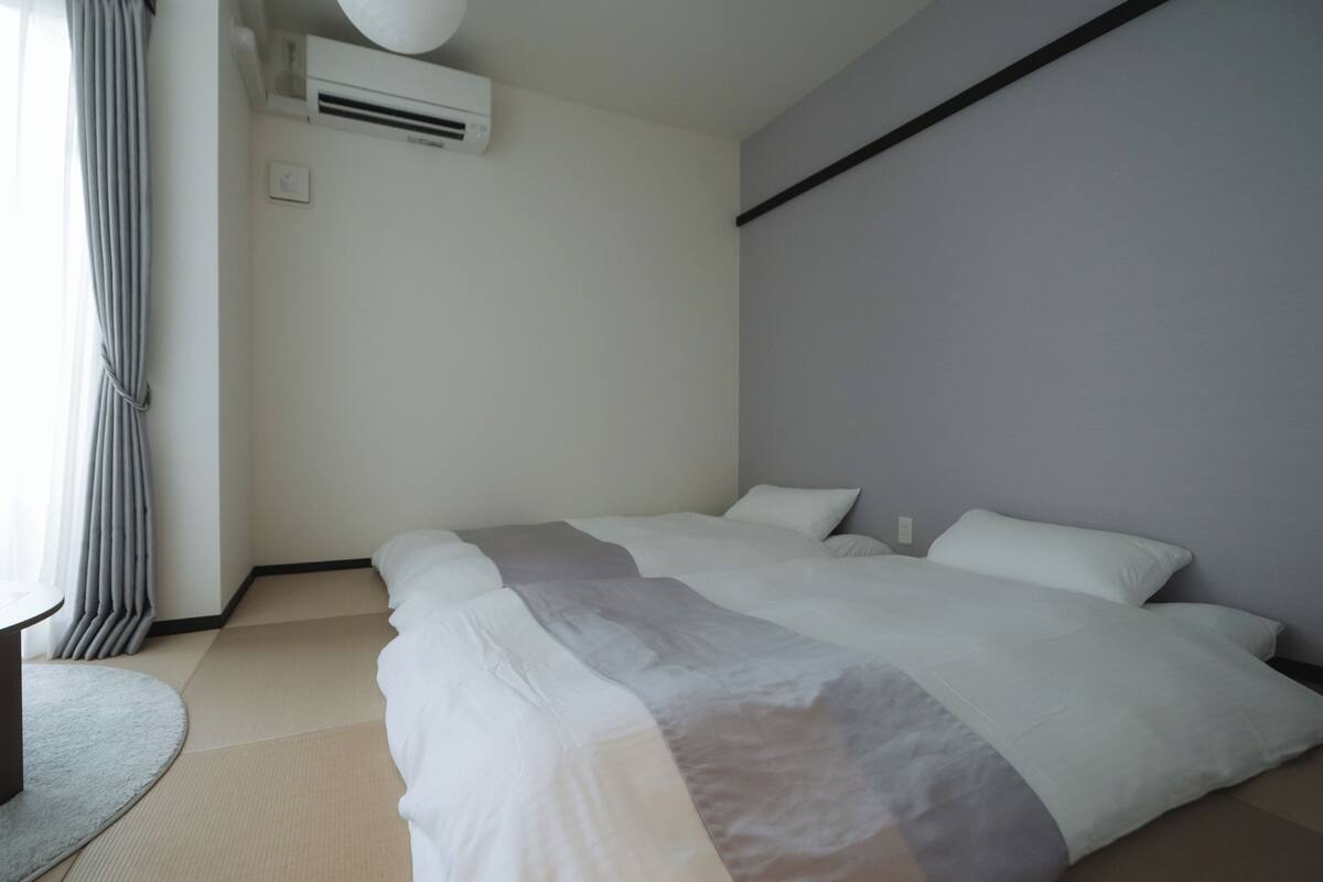 A hotel room with a bed, a round table, a wall-mounted air conditioner, and a curtain.