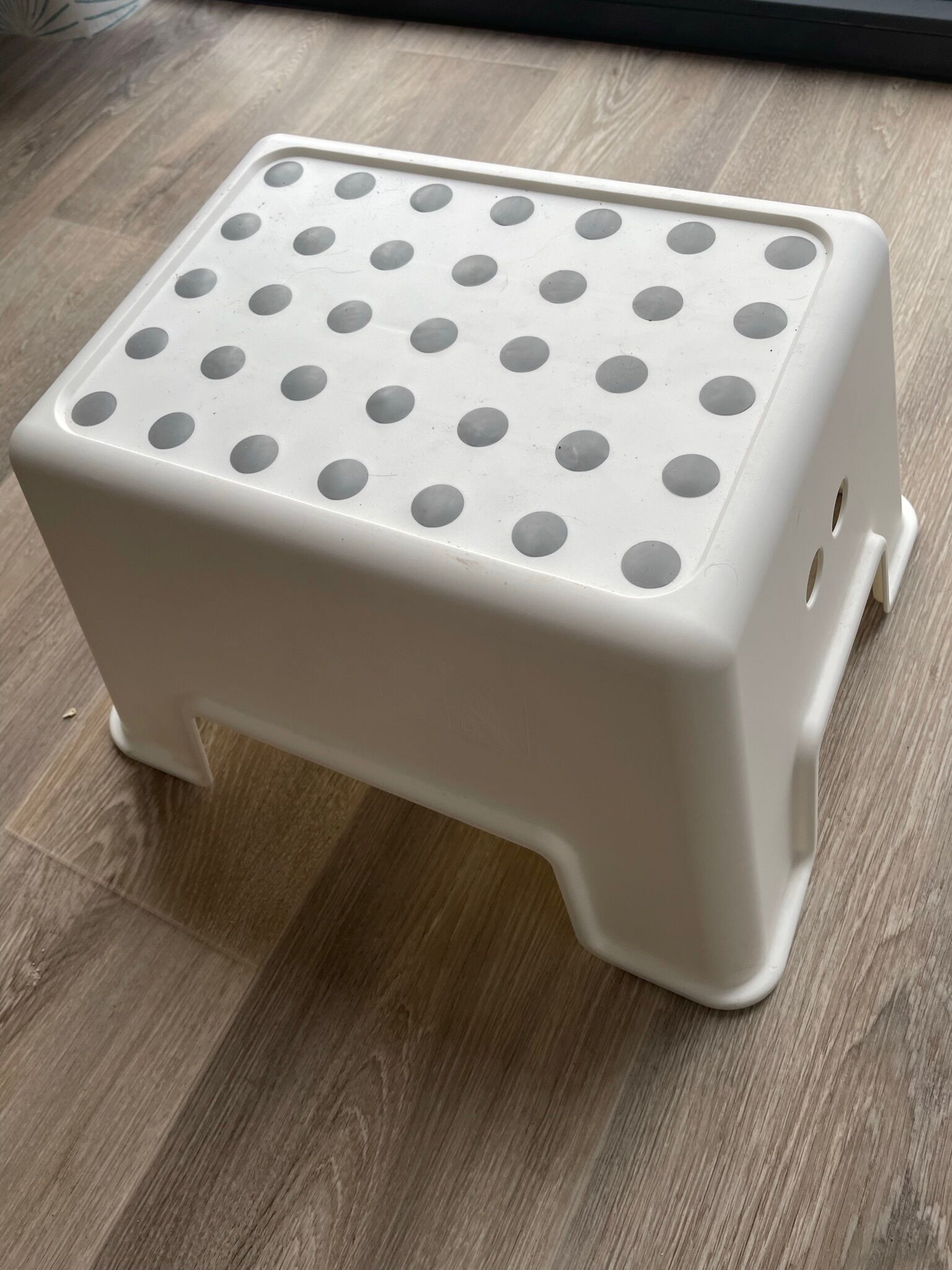 A white plastic step with a perforated top, placed on a wooden floor.