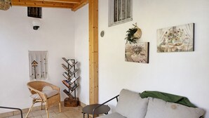 Una habitación acogedora con un sofá, una silla de mimbre, una mesita pequeña y una estantería.