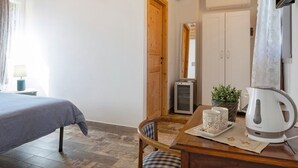 Ein Zimmer mit einem Bett, einem Holztisch mit Wasserkocher, Tassen und einer kleinen Pflanze.