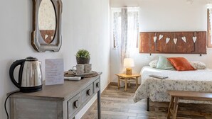 A bedroom with a bed, a bedside table with a lamp, a wooden headboard with heart decorations, a dresser with a kettle, and a mirror. - Room 3 – Spacious Double Room with Shared Pool, Wi-Fi, and Air Conditioning (Cavaion Veronese)