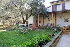 A garden with outdoor seating, a tree, and a building with wooden shutters. - Double Room '4' with Shared Pool, Wi-Fi and Air Conditioning (Cavaion Veronese)