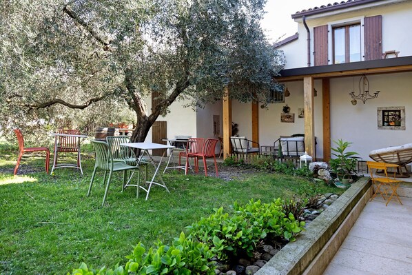 A garden with outdoor seating, a tree, and a building with wooden shutters. - Double Room '4' with Shared Pool, Wi-Fi and Air Conditioning (Cavaion Veronese)