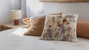 Un letto con cuscini a motivi floreali, una lampada da comodino e uno scaffale con oggetti decorativi.