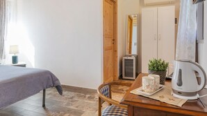 Quarto com cama, uma mesa de madeira com chaleira, xícaras e um vaso de planta.