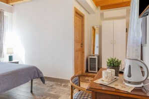 Ein Schlafzimmer mit einem Bett, einem Holztisch mit Wasserkocher, Tassen und einer Blumentopfpflanze.