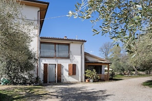 A two-story house with a balcony, a gravel driveway, and surrounding vegetation. - Room 6 – Spacious Double with Shared Pool, Wi-Fi, and Air Conditioning (Cavaion Veronese)