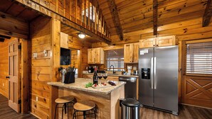 Una cocina estilo cabaña de madera con una isla central, taburetes de bar, electrodomésticos de acero inoxidable y armarios de madera.