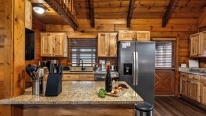 Una cocina con gabinetes de madera, encimeras de granito, un refrigerador de acero inoxidable y un horno empotrado.