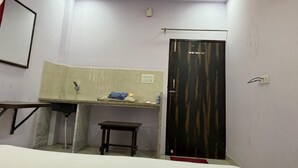 A small, well-lit room with a sink, a mirror, a door, and a small table. - Hotel The Gold by Yatrik Hotels (Jaipur)