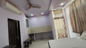 A bedroom with a bed, a desk, a bench, a ceiling fan, and a window with curtains. - Hotel The Gold by Yatrik Hotels (Jaipur)