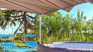 A covered outdoor area with a large wicker hot tub, two lounge chairs, and artificial grass. - Mary Jungle (Sant'Elpidio a Mare)