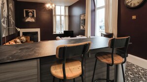 A modern living room with a dark wood floor, a central seating area with a sofa and two chairs, a fireplace, and a large wall clock. - The Hyde (Preston)