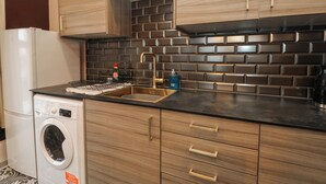 A compact kitchen with wooden cabinets, a built-in dishwasher, and a stainless steel sink. - The Hyde (Preston)
