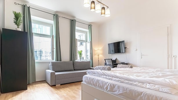 Quarto moderno com cama, sofá, televisão e escrivaninha.