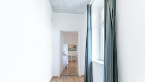 Um corredor com piso de madeira que leva a uma sala de jantar com mobiliário branco.