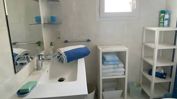 Een badkamer met een wastafel, spiegel, planken en een raam.