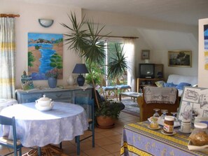 A cozy living room with a dining area, a television, and a large window with a view. - Guest Room "Les Hortensias" with Shared Terrace, Private Garden and Wi-Fi (Perros Guirec)