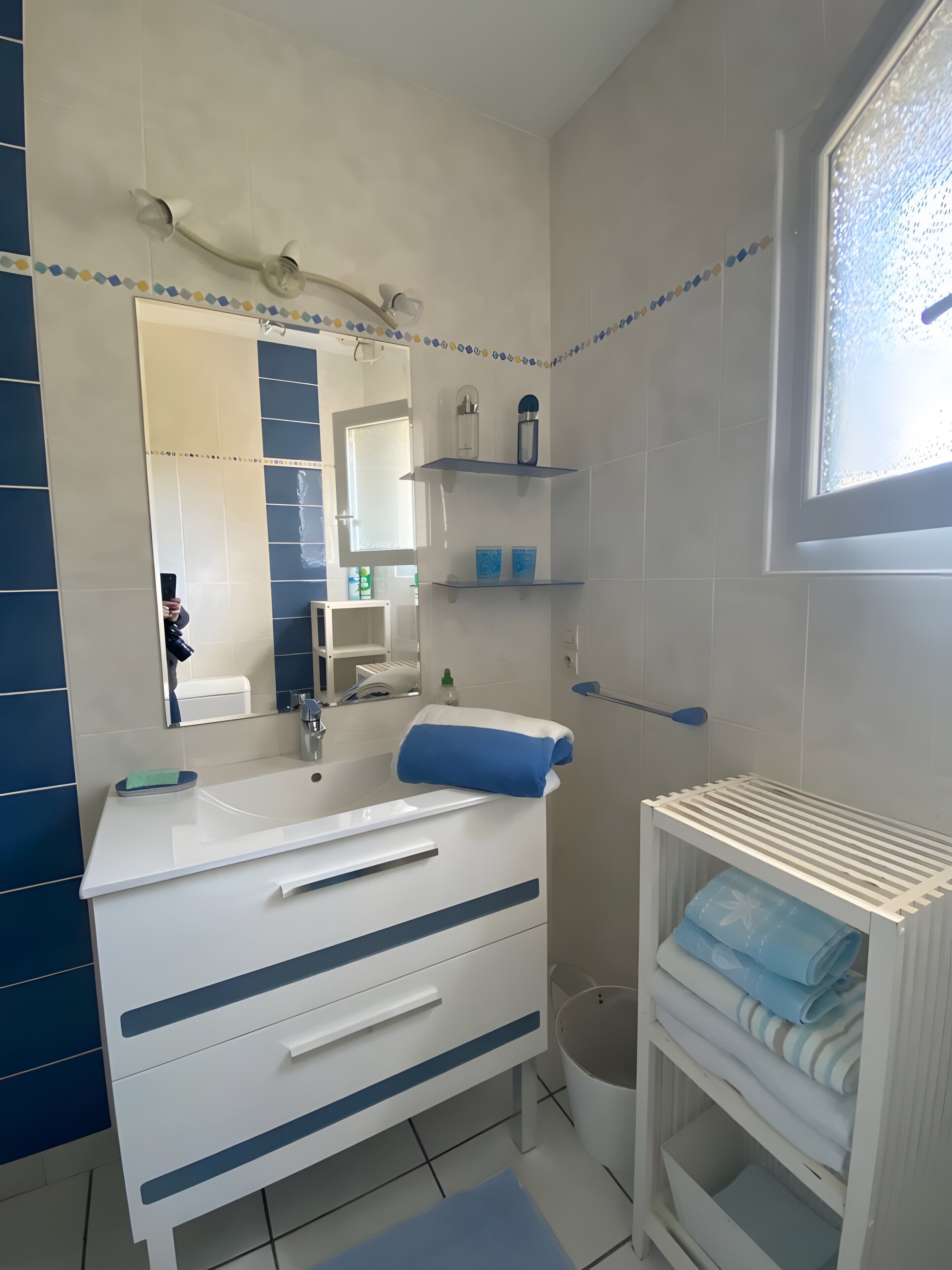 Een badkamer met een wit wastafelmeubel, een spiegel, een handdoekrek en een plank met toiletartikelen.