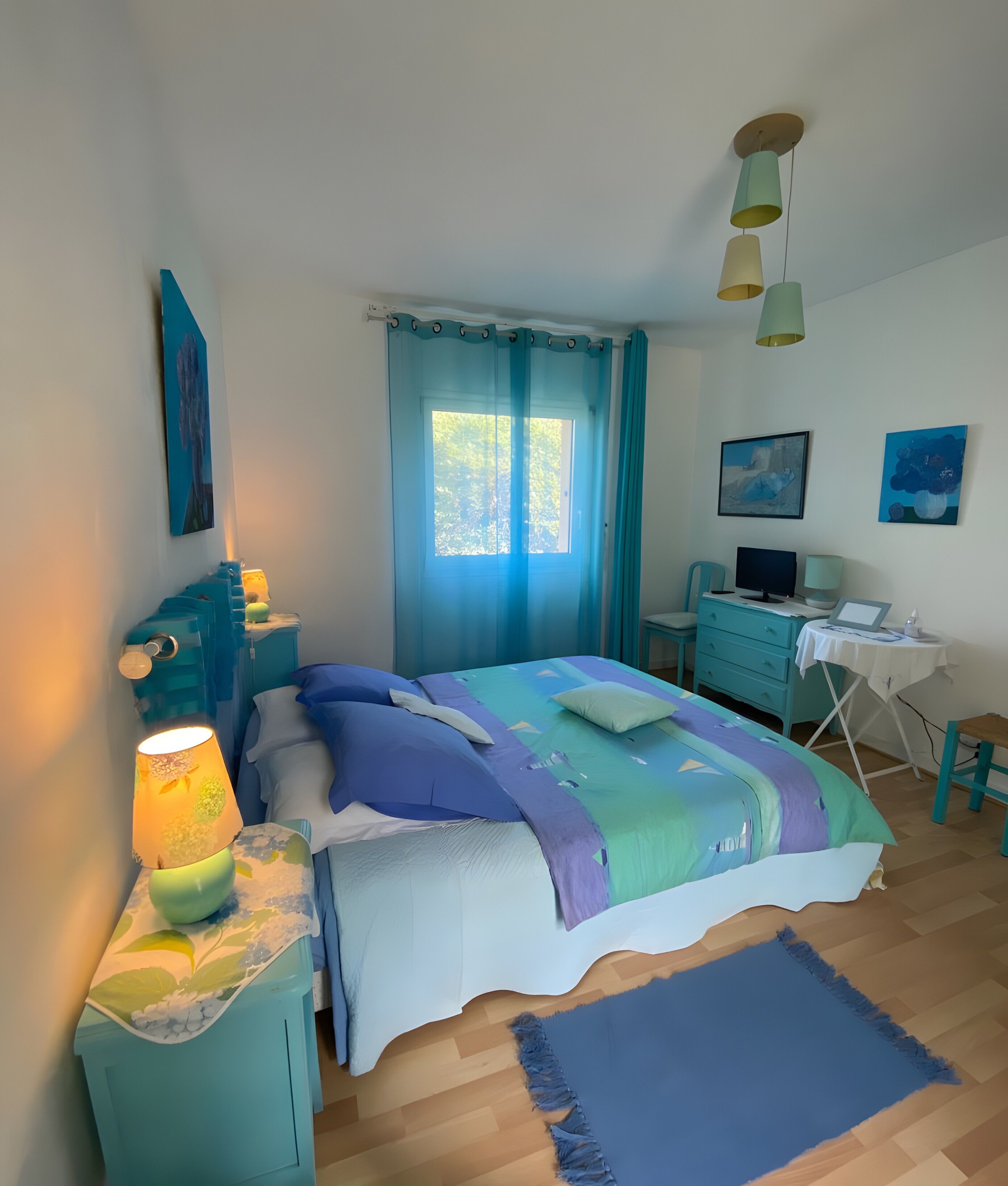 A bedroom with a bed, a desk, a chair, a lamp, and a window with curtains.