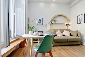 Ein modernes Wohnzimmer mit einem runden Tisch, einem grünen Sessel, einem beigen Sofa und einer hölzernen Bank.
