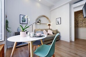 Ein modernes Wohnzimmer mit einem runden weißen Tisch, türkisfarbenen Sesseln, einem grauen Sofa und einer Ziegelwand.