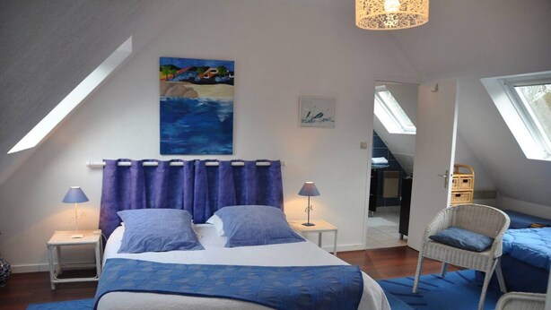 Ein Schlafzimmer mit einem großen Bett, zwei Nachttischen, einem Sessel, einem Gemälde und einem Oberlicht.