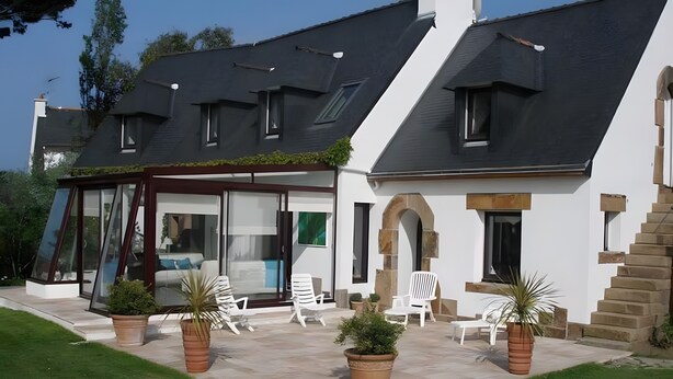 Une maison moderne dotée d’un patio, de chaises blanches et de plantes en pot.