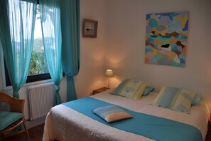 Une chambre à coucher avec un lit, des rideaux, un radiateur, une lampe, une chaise et un tableau accroché au mur.