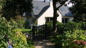 Un chemin menant à une maison dotée d’une entrée fermée par un portail, entourée d’une végétation luxuriante et d’un jardin bien entretenu.