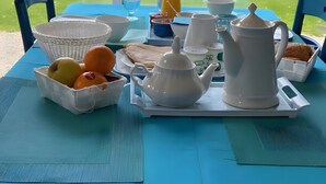 Une table mise pour le petit-déjeuner, avec une théière, des tasses, un bol de fruits et un vase de fleurs.