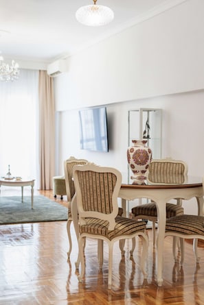 A dining area with a round table and six chairs, a chandelier, a vase, and a television on the wall. - Erato by halu! - Classical 2BD penthouse in the center (Thessaloniki)