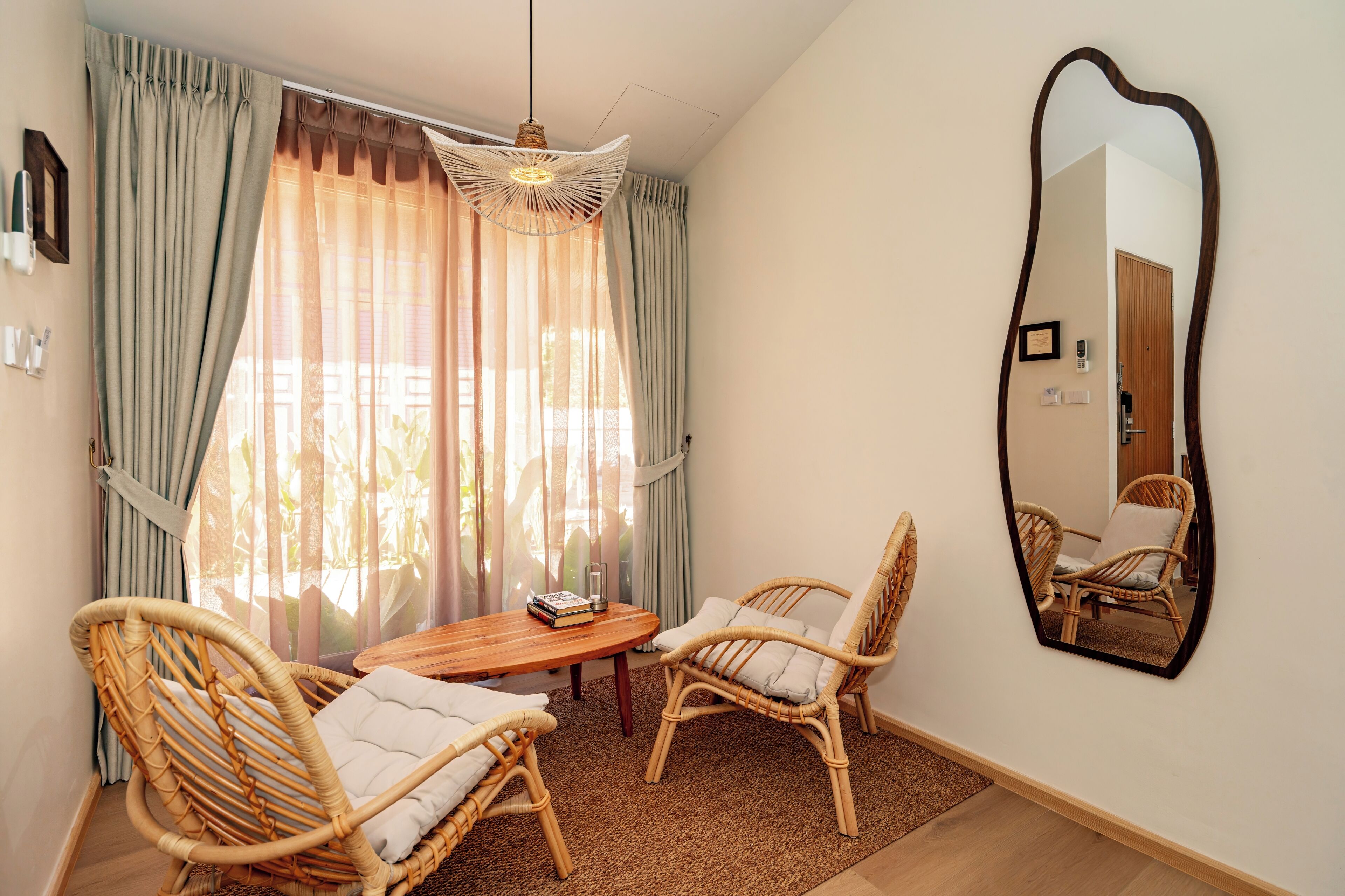 A room with a dining table, two wicker chairs, a mirror, and a window with curtains.