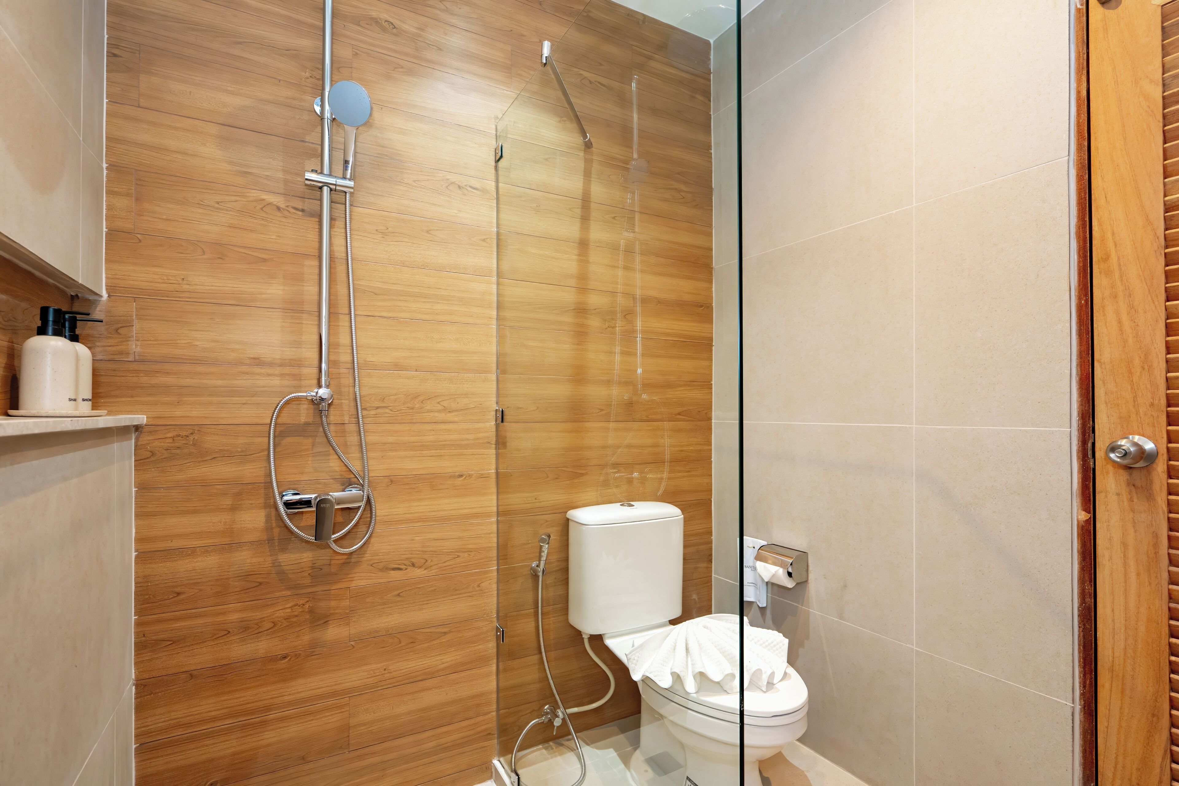 Ein modernes Badezimmer mit einer Holzwand, einer Duschkabine aus Glas und einem WC mit einem weißen Toilettenpapierhalter.