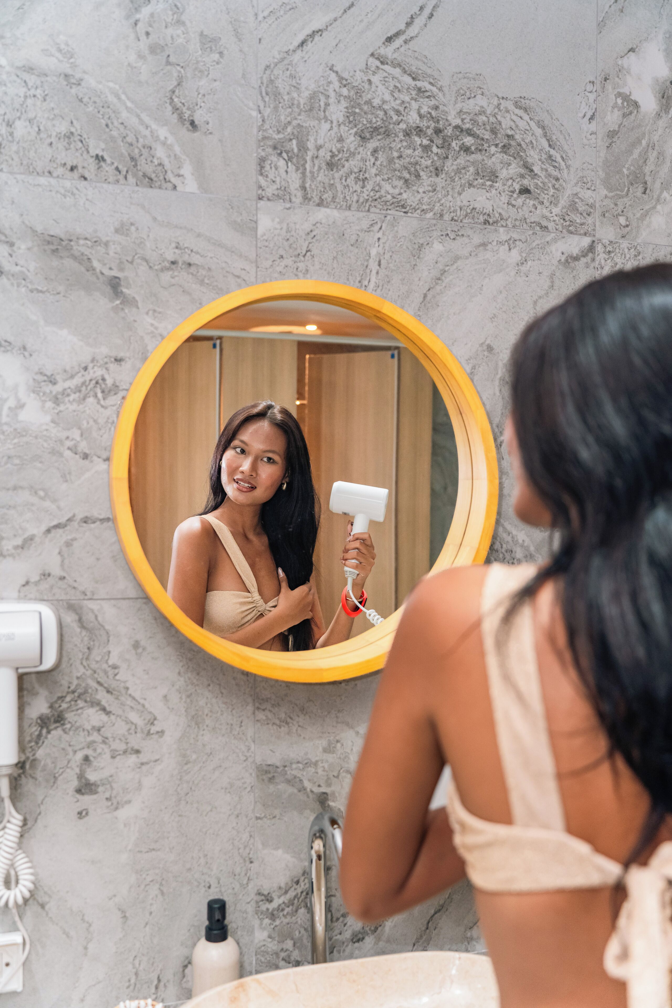 Un baño con pared de mármol, un espejo redondo, un lavabo y un secador de pelo.