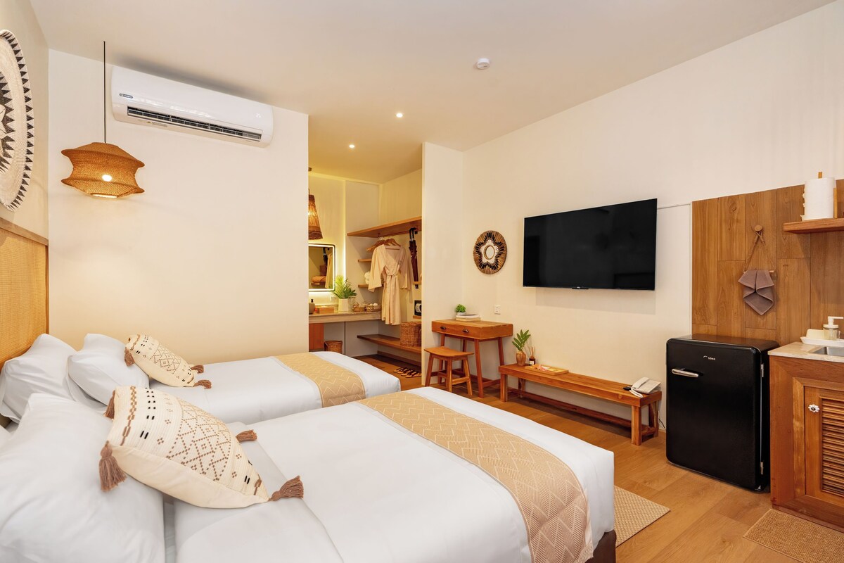 A hotel room with two beds, a TV, a refrigerator, a desk, and a bathroom.