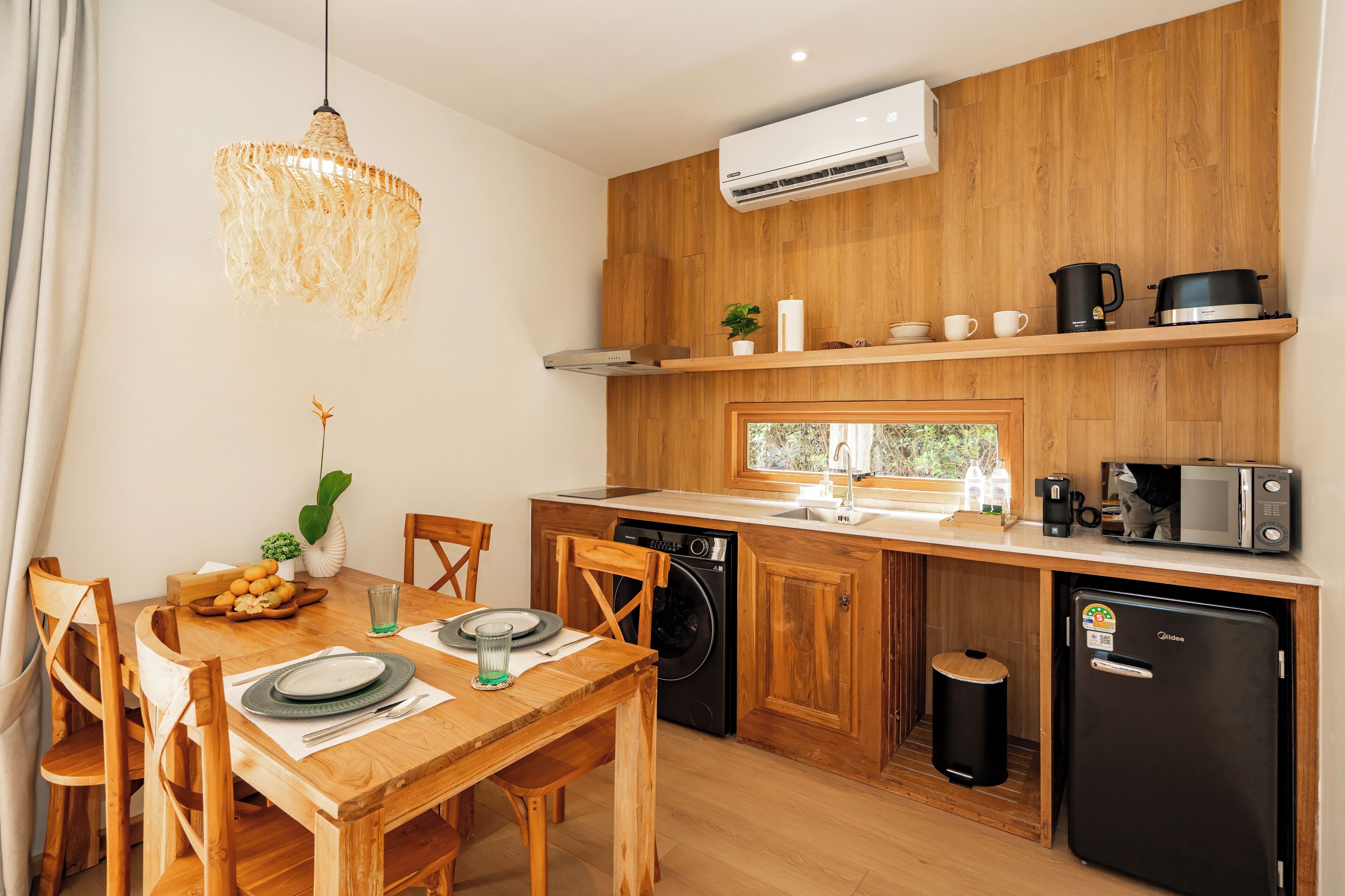 A compact kitchen with wooden cabinets, a built-in dishwasher, a refrigerator, and a window overlooking greenery.