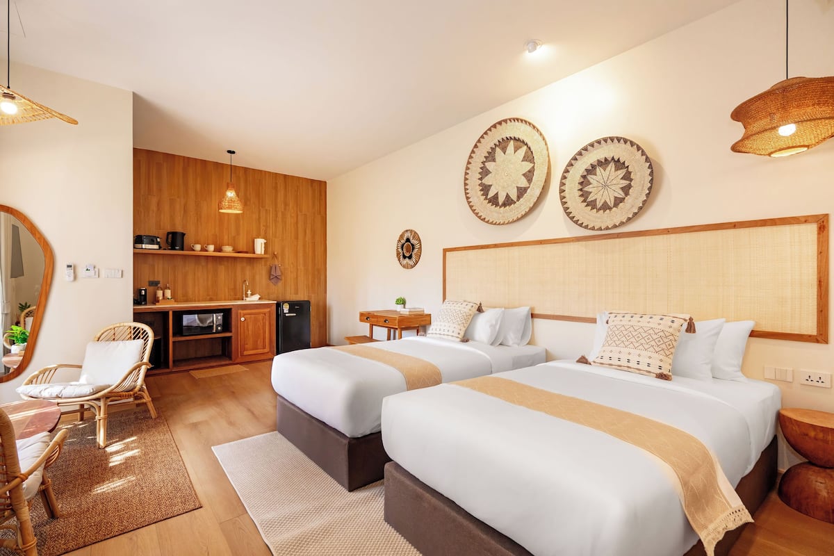 Habitación de hotel con dos camas, un armario de madera, una pequeña cocina y una mesa de comedor.