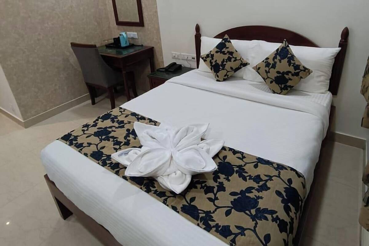 Una cama bien hecha con ropa de cama floral, una mesita de noche con lámpara y un espejo en la pared.