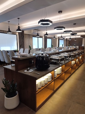 A modern buffet setup with a central island, multiple seating areas, and pendant lighting.