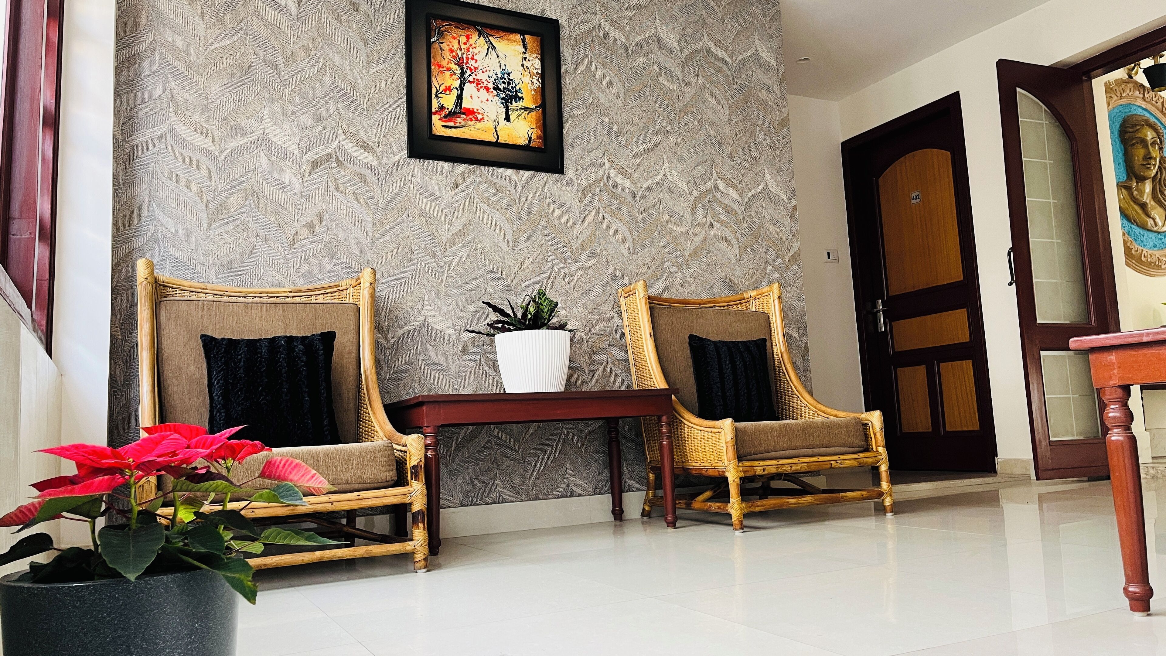 A room with two wicker chairs, a small table with a potted plant, and a framed artwork on the wall.