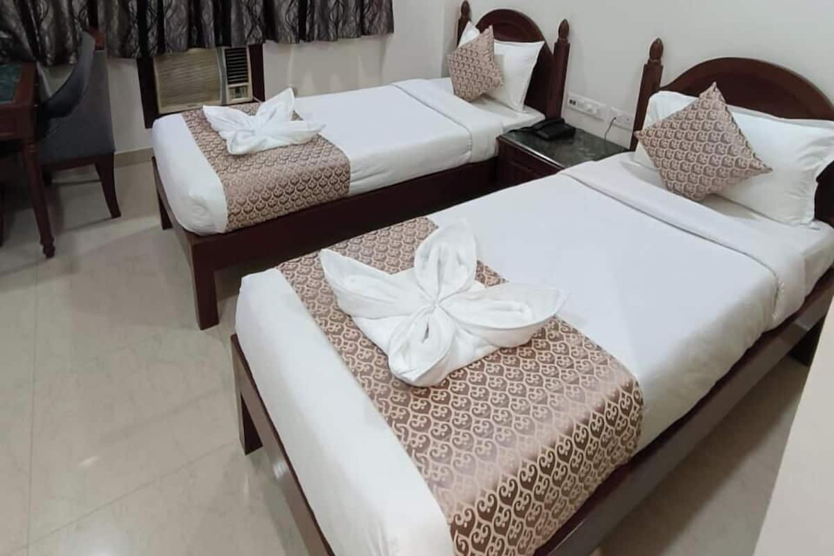 Habitación de hotel con dos camas, ventilador de techo y ventana con cortinas estampadas.