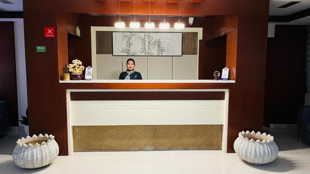 A reception desk with a receptionist, a framed artwork above, and two decorative planters.