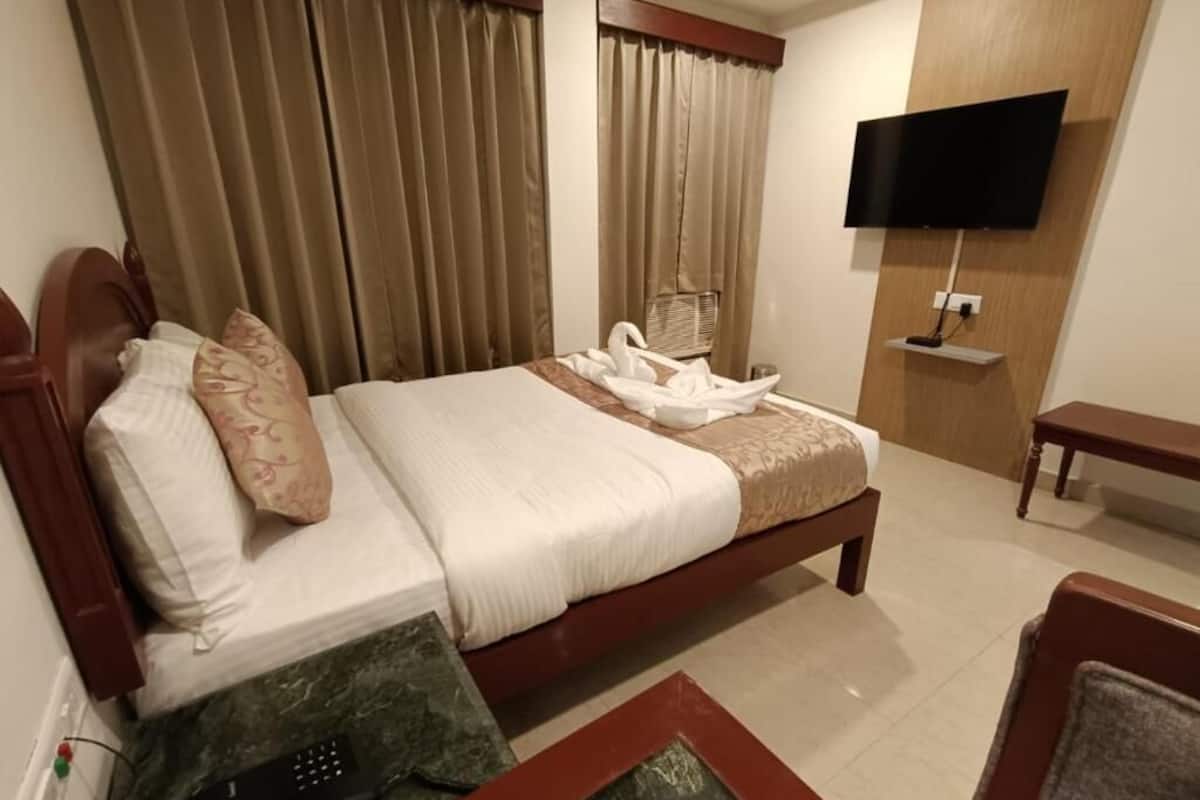 Una habitación de hotel con una cama, un televisor montado en la pared, un escritorio y una silla.