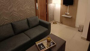Un salon moderne avec un canapé vert, une table basse avec un plateau, une lampe et un téléviseur fixé au mur.