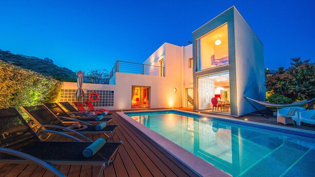 A modern house with a swimming pool, lounge chairs, and a dining area.