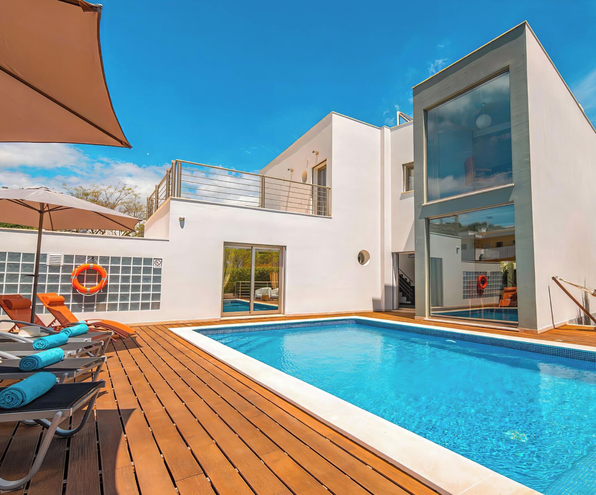 Ein moderner Poolbereich mit Holzterrasse, Liegestühlen und einem klaren, blauen Pool.